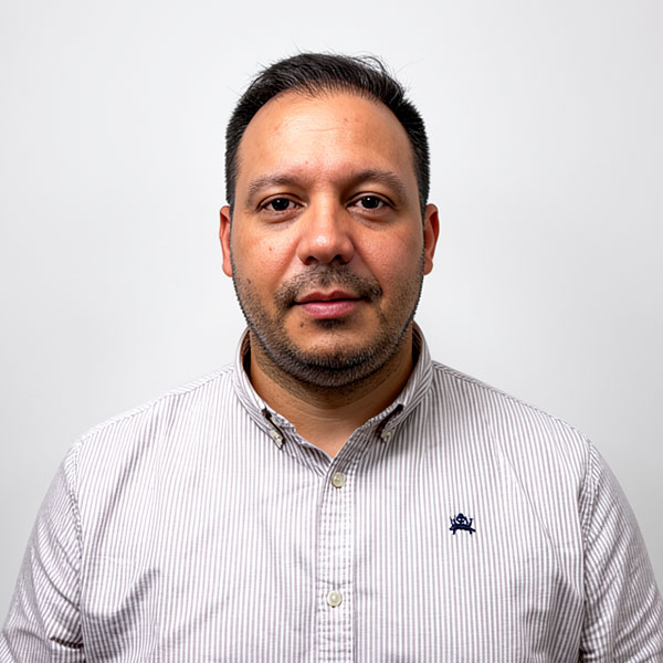 Portrait of a man with short dark hair and light stubble, wearing a light striped button-down shirt, facing the camera.