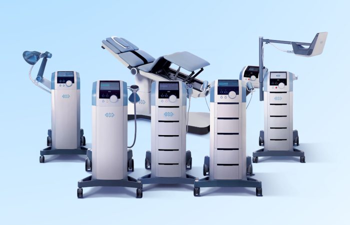 Row of modern anesthesia/medical ventilator machines on wheeled carts against a pale blue background.
