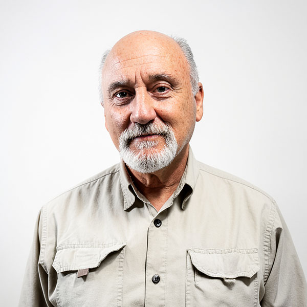 Portrait of an older man with a white beard and mustache, wearing a beige button-down shirt against a light background.