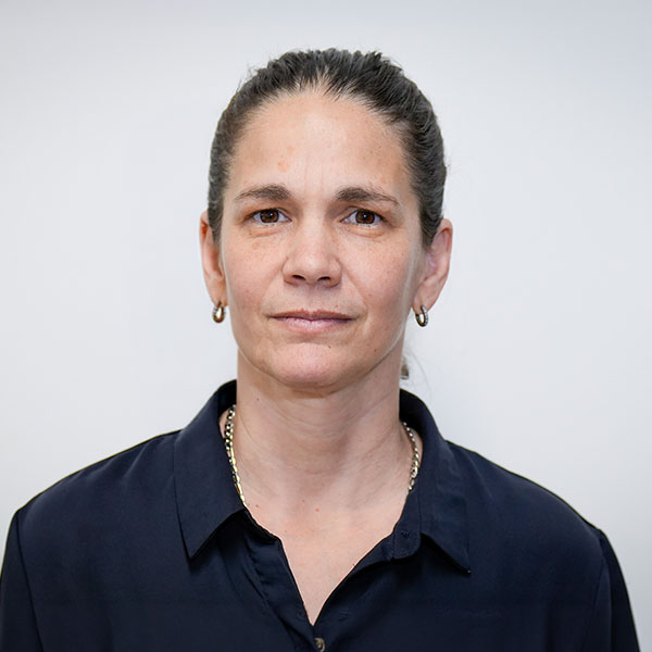 Portrait of a woman with dark hair tied back, wearing a navy button-down shirt, with a neutral expression against a light background.