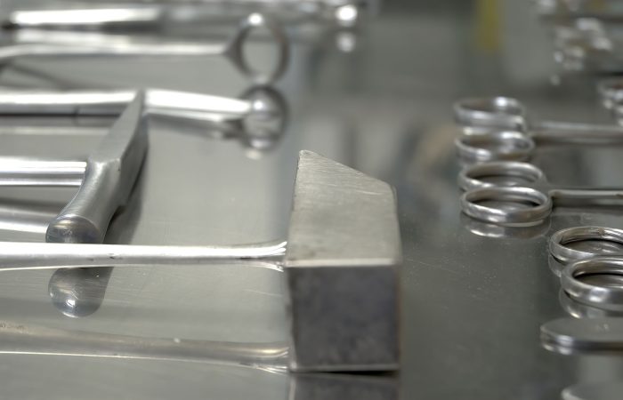 Close-up of shiny stainless steel surgical instruments laid on a reflective metal tray.