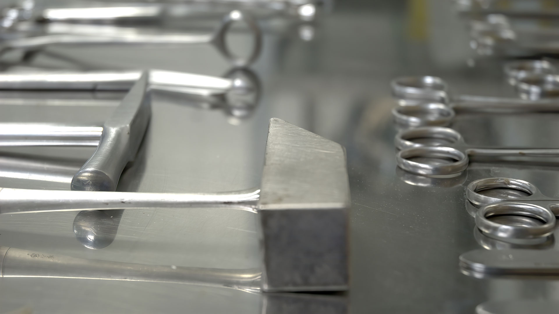 Close-up of shiny stainless steel surgical instruments laid on a reflective metal tray.