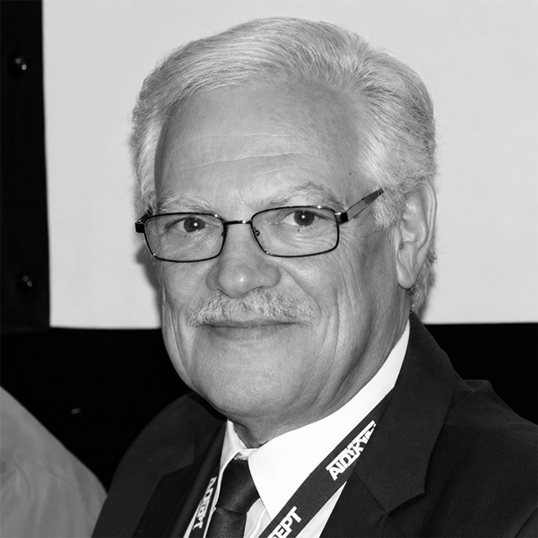 Portrait of an older man with gray hair and a mustache, wearing glasses, a suit, and a lanyard.