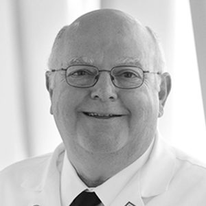 Smiling older man in white uniform and glasses, looking at the camera.