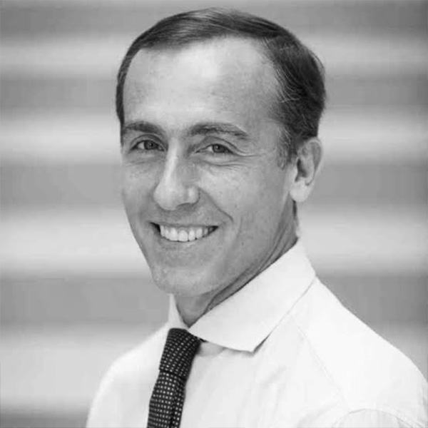 Black-and-white head-and-shoulders portrait of a smiling man in a white shirt and dark tie.