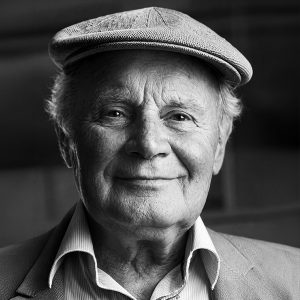 Smiling elderly man wearing a flat cap and blazer, looking at the camera.
