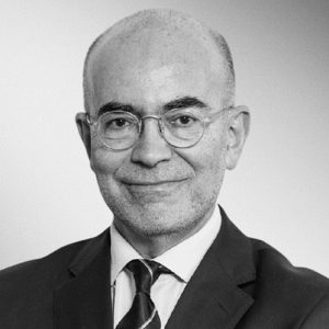 Professional head-and-shoulders portrait of a smiling man in a suit and tie, wearing round glasses.