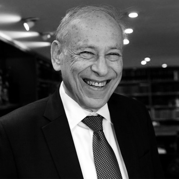 Smiling older man in a dark suit and polka-dot tie, in a professional setting.