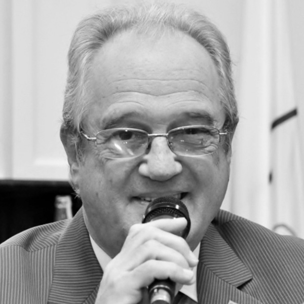 Older man in a suit speaks into a handheld microphone.