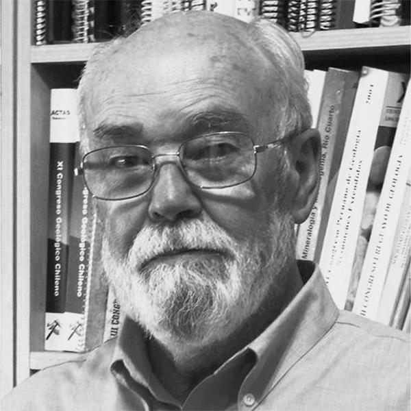 Portrait of an older man with gray hair and a white beard wearing glasses, in front of a bookshelf filled with books and journals.