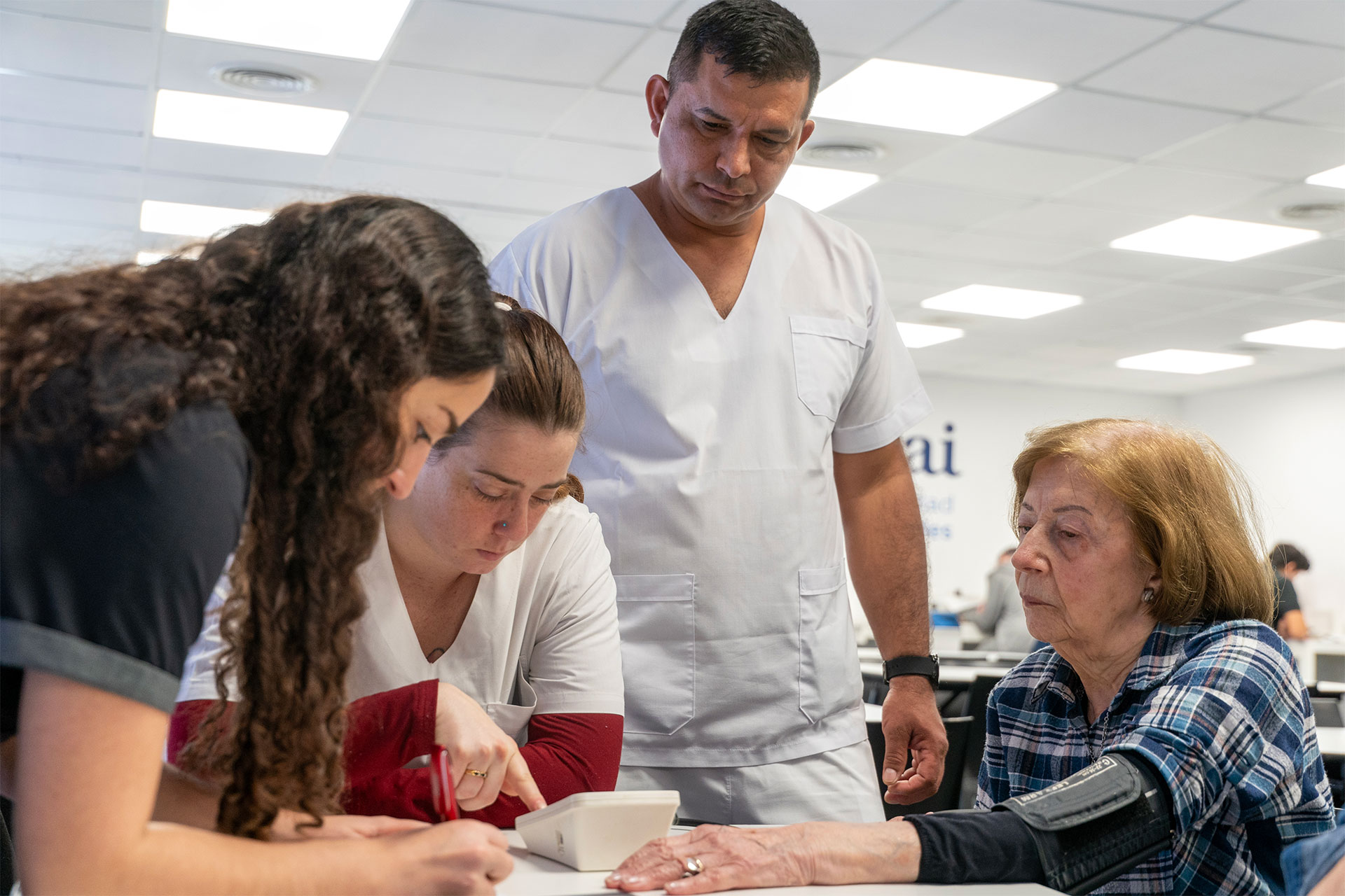 Nurse in white scrubs measures an elderly woman's blood pressure at a clinic desk while others look on.