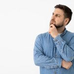 Thoughtful man in a denim shirt with his hand on his chin looking up as if pondering a question