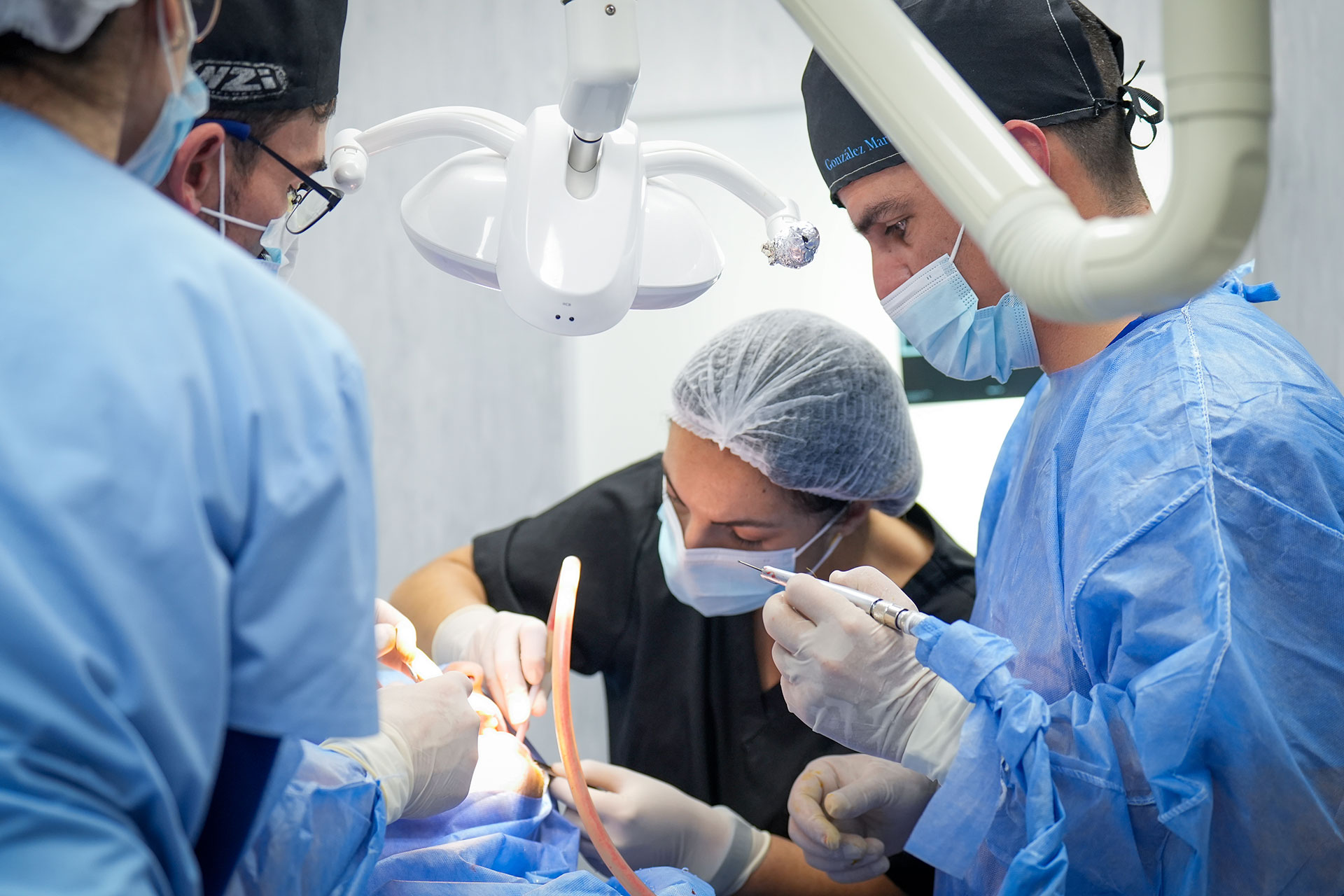 Team of surgeons in blue gowns performing an operation, wearing masks and caps under bright overhead lights.