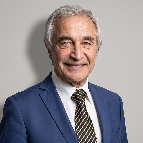 Smiling older man in a blue suit and striped tie poses for a professional portrait.