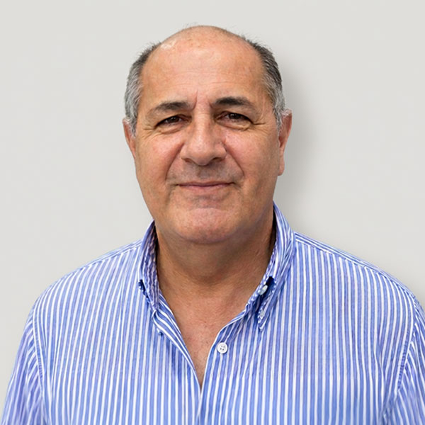 Portrait of a smiling middle-aged man with short gray hair wearing a blue striped shirt against a light gray background.