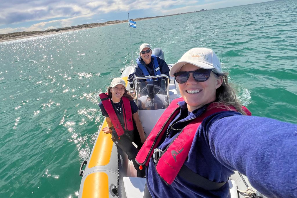 2026092221ConMagdalenaAriasImagen2 UMAI Three people wearing red life jackets pose for a selfie on a small inflatable boat in turquoise water coastline in the background